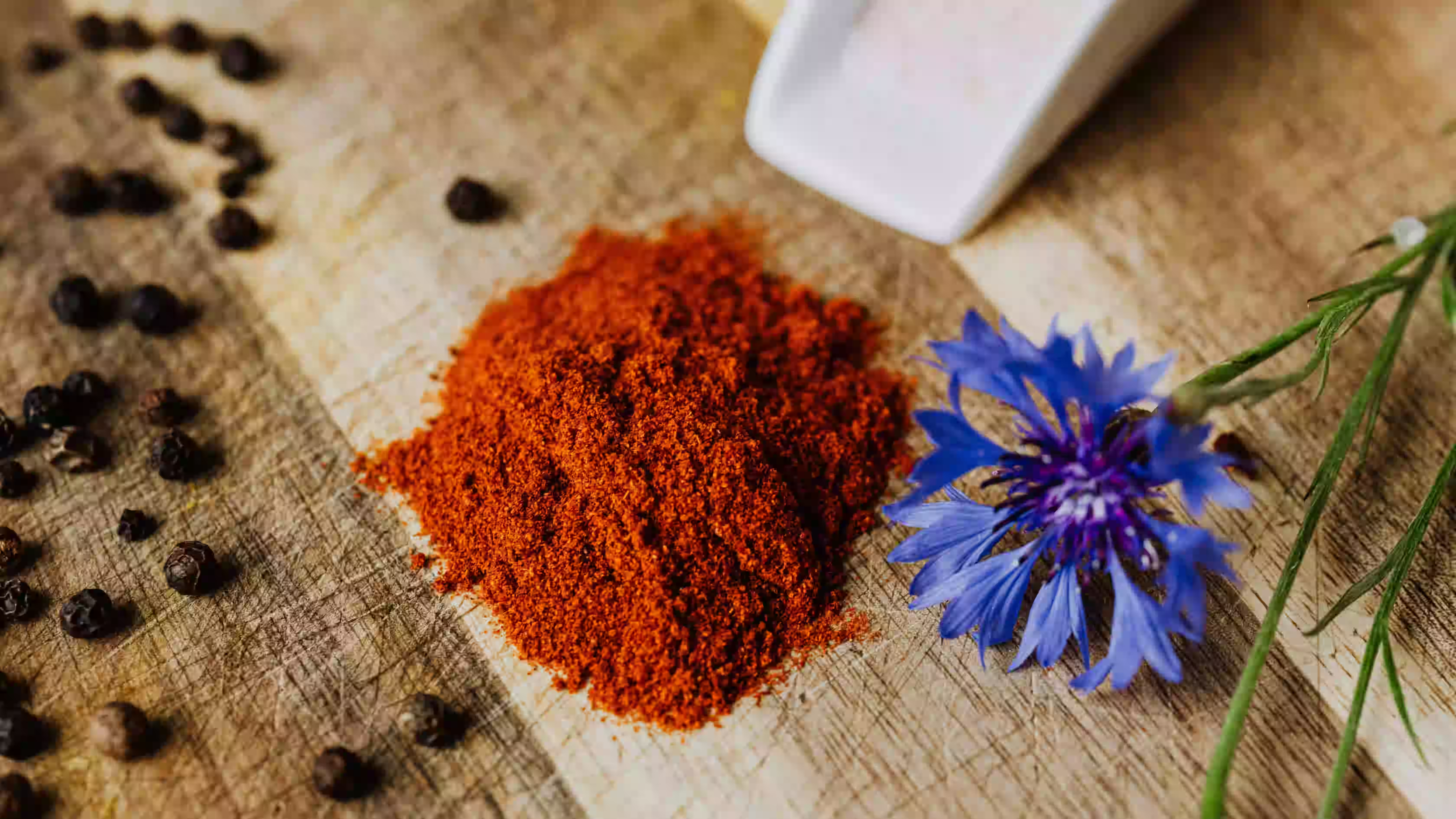 Vibrant red annatto powder for authentic annatto seasoning recipes alongside spicy peppercorns and a blue flower